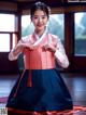 A woman in a pink and blue hanbok poses for a picture.