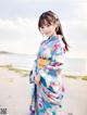 A woman in a blue kimono standing on a beach.